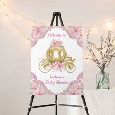 a welcome baby shower sign on an easel next to a vase with flowers and lights