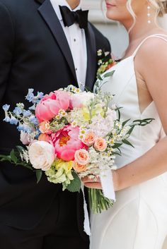 a bride and groom pose for a wedding photo in their tuxedo attire, holding a bouquet of flowers