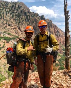 two men in hard hats and safety gear standing next to each other on the side of a mountain