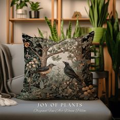 a pillow with two birds on it sitting on a couch next to a potted plant