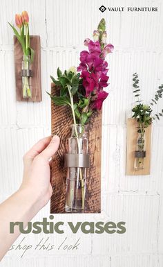 a hand holding a vase with flowers in it on a wooden wall mounted shelf next to two flower pots