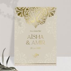 an elegant wedding card with gold foil on the front and back, sitting next to a plant