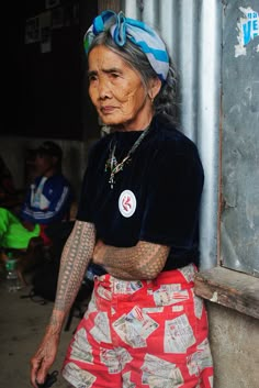 an old woman with tattoos on her arm and chest sitting in front of a building