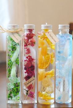 four bottles filled with different types of flowers and herbs sitting on top of a wooden table