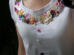 a woman wearing a white shirt with colorful buttons on it's collar and necklace