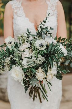 a bride holding a bouquet of white flowers and greenery