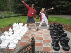 two people standing in front of a giant chess set on top of a brick walkway