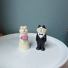 two wedding cats sitting on top of a white table next to each other and one is wearing a tuxedo