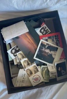 an open suitcase filled with lots of photos and papers on top of a white sheet