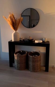 a black table with two baskets and a round mirror on the wall behind it,