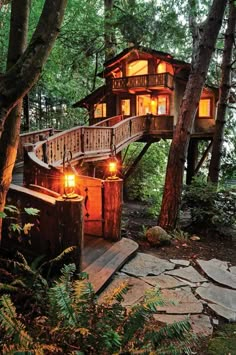 a tree house in the woods with stairs leading up to it and lights shining from windows