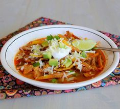 a white bowl filled with food on top of a colorful place mat next to a spoon