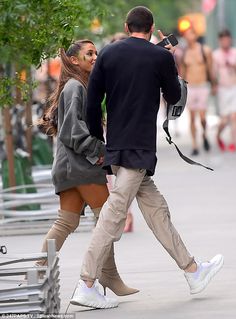 the man and woman are walking down the street together, one is taking a photo