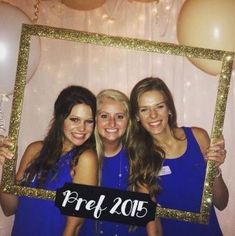 three beautiful young women standing next to each other in front of a photo booth with balloons