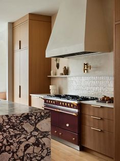 a kitchen with marble counter tops and wooden cabinets, along with an oven hood over the stove