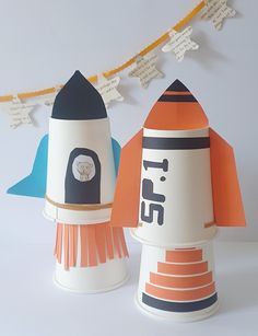 two paper rockets sitting next to each other on top of a white table with bunting