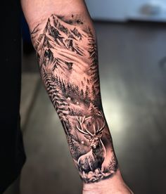 a man's arm with a deer and mountain scene tattoo on the left forearm