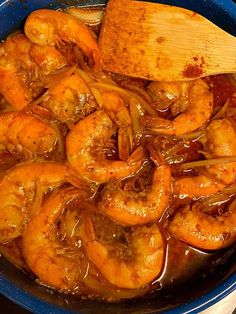 cooked shrimp in sauce with wooden spoon in blue bowl on stove top next to utensils