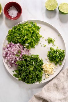 chopped up vegetables on a white plate next to limes and other ingredients for the dish