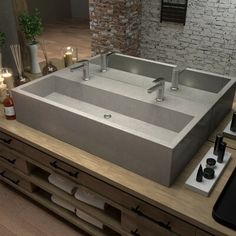 a large rectangular stone sink on top of a wooden counter next to candles and bottles