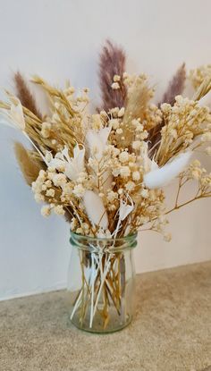 dried flowers in a glass jar on a countertop with white walls behind it and beige flooring