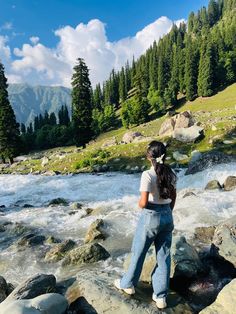 a woman standing on top of a rock next to a river