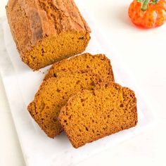 three slices of pumpkin bread on a white platter next to a small orange tomato