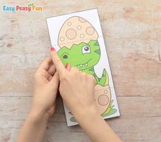 a person holding up a coloring book with an egg in the shape of a dinosaur