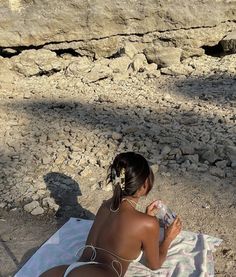 a woman sitting on top of a towel next to rocks