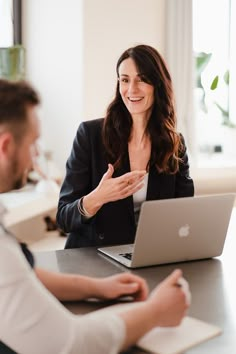 a woman sitting in front of a laptop computer talking to another person at a table