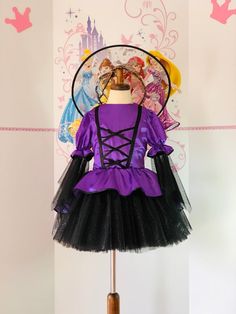 a purple dress with black tulle and bows is on display in front of a wall