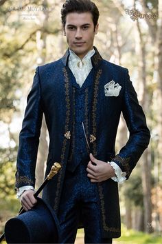 Baroque period groom suit, fitted jacket with Napoleon collar in blue jacquard fabric, with gold embroidery and crystal brooch. Baroque groom suit model 2069 Mario Moyano perfect custom tailoring for men's weddings. Best groom suit shops specialising in different and original themed weddings. Tailor-made suits with a modern slim cut, suits for bold and informal men, elegant looks with a baroque idea. Groom Suit Royal Blue, Prince Groom Suit, Royal Attire Men, Best Groom Suits, Groom Suit Vintage, Collar Frock, Victorian Prom, Wedding Morning Suits, Royal Suit