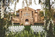 an outdoor ceremony with white chairs and greenery in front of a large stone building