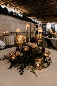 candles and flowers on a white table cloth with greenery in front of the centerpiece