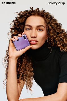 a woman with curly hair holding a cell phone in her hand and looking at the camera