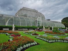 a large greenhouse with many plants and flowers in the ground around it on a cloudy day