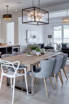 a dining room table with chairs and lights hanging from it's ceiling in front of an open kitchen