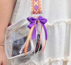 a woman is holding a clear bag with purple ribbon and beads on the front pocket