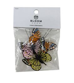 three colorful butterflies in plastic packaging on a white background with the words bloom printed on it