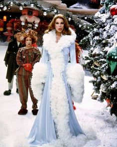 a woman in a long blue dress with white fur on her shoulders and two men standing behind her