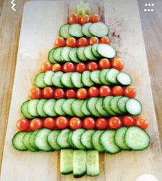 a christmas tree made out of cucumbers and tomatoes on a wooden cutting board