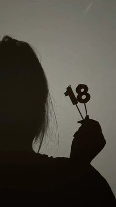 the silhouette of a person holding up a small number eight stick in front of their face