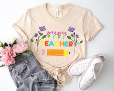 a t - shirt with the words teacher written on it next to some jeans and flowers