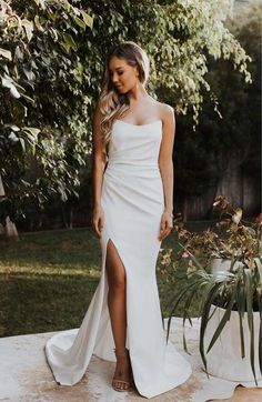 a woman wearing a white wedding dress with a slit down the side and one leg