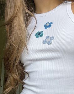 a close up of a person wearing a white tank top with blue flowers on it