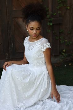 a woman in a white dress sitting on the ground with her hand on her knee