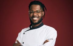 a man wearing glasses and a chef's coat poses for a photo in front of a red background