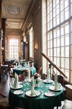 a dining room filled with lots of tables covered in green cloths and place settings