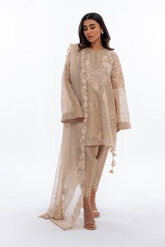 A short beige khaddi corduroy shirt with aari and tilla embroidery is paired with a matching worked organza dupatta. Playful tassel detailing complements the shirt and an embroidered rawsilk shalwar completes the look. Model Height is 5'2 and Shirt Length is 35' Suit Necklines Indian, Elegant Kurtis Classy, Beige Salwar Suit, Co Ords Outfits Pakistani, New Pakistani Suit Design, Organza Suit Design, Pakistani Casual Suits, Organza Outfit, Tilla Embroidery