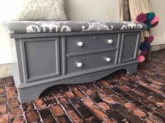 a gray bench sitting on top of a brick floor next to a pillow and stuffed animal